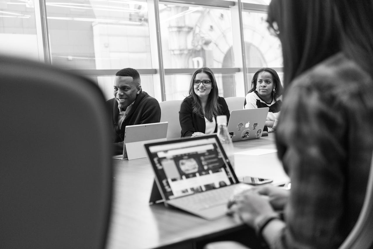 Diverse team of adults engaged in a meeting using laptops in a modern office setting.